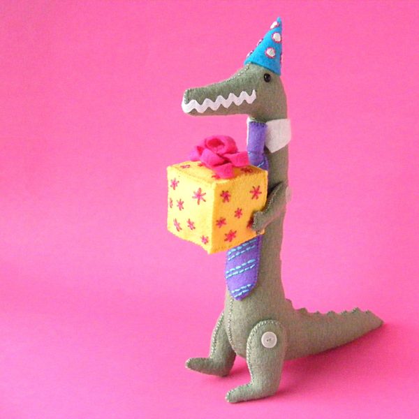felt crocodile with button joints wearing a birthday hat and carrying a gift - made with the Carlisle Crocodile pattern from Shiny Happy World