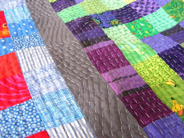 Close-up of Big Stitch Quilting (using running stitch) on a colorful scrap quilt.