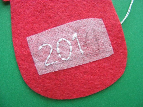 partially embroidered date on the back of a felt ornament using the free alphabet embroidery pattern from Shiny Happy World