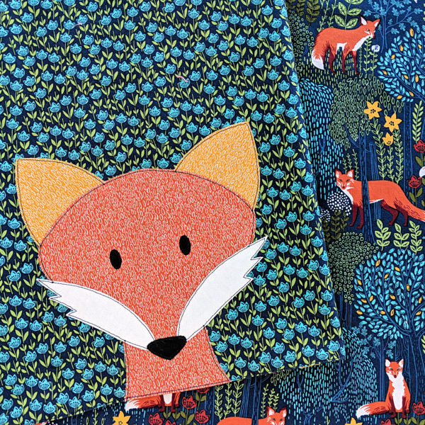 applique fox on blue floral background, with a large scale multicolored fox print behind that - demonstrating how to choose fabric for a quilt