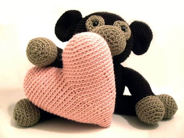 Soft crocheted monkey holding a pink heart plush toy, perfect for children’s toys and nursery decor.