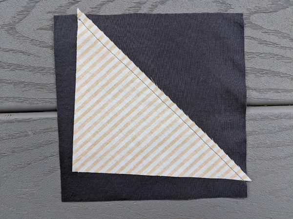 Triangle sewn unevenly to a grey square - making one corner of a wonky churn dash block 