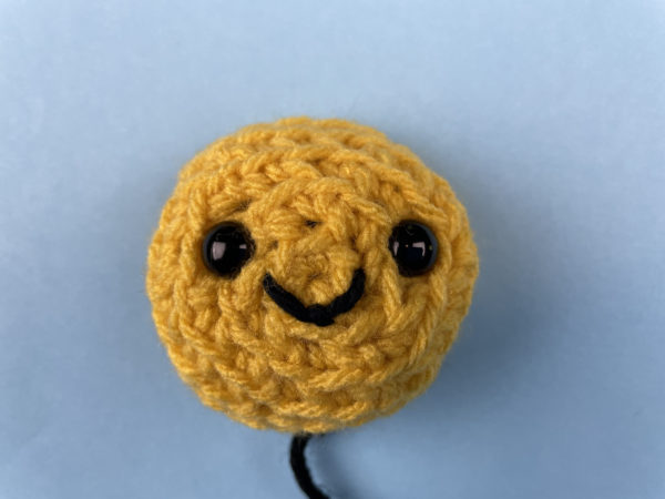 crocheted bee face with plastic craft eyes and an embroidered smile