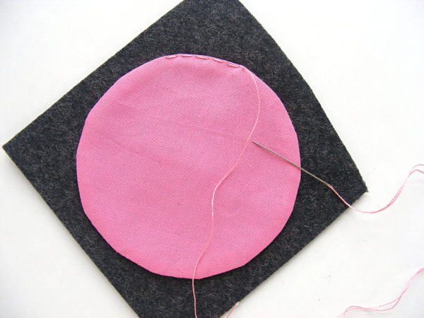 Making Polkadot Felt Coasters - sewing a pink circle of fabric to grey felt using a running stitch and matching thread.