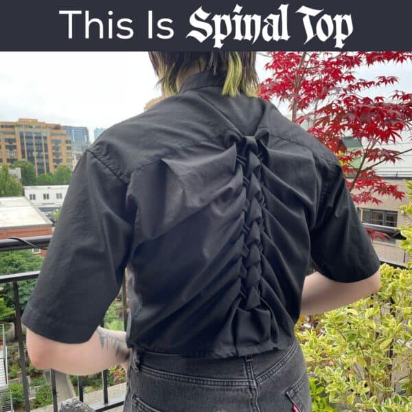 Black shirt with smocked back spine design, outdoor urban setting, red and green foliage.